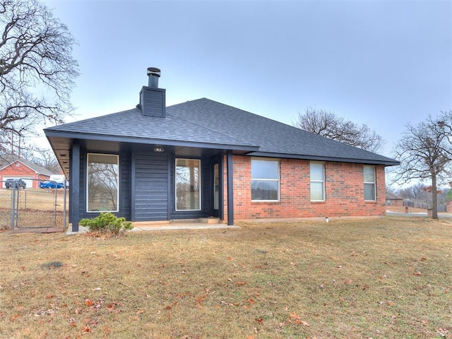 back of property with a shingled roof, a chimney, a lawn, and brick siding