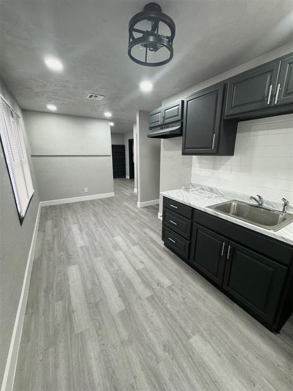 kitchen featuring tasteful backsplash, light stone countertops, sink, and light hardwood / wood-style floors