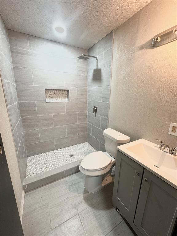 bathroom with vanity, a textured ceiling, toilet, and tiled shower