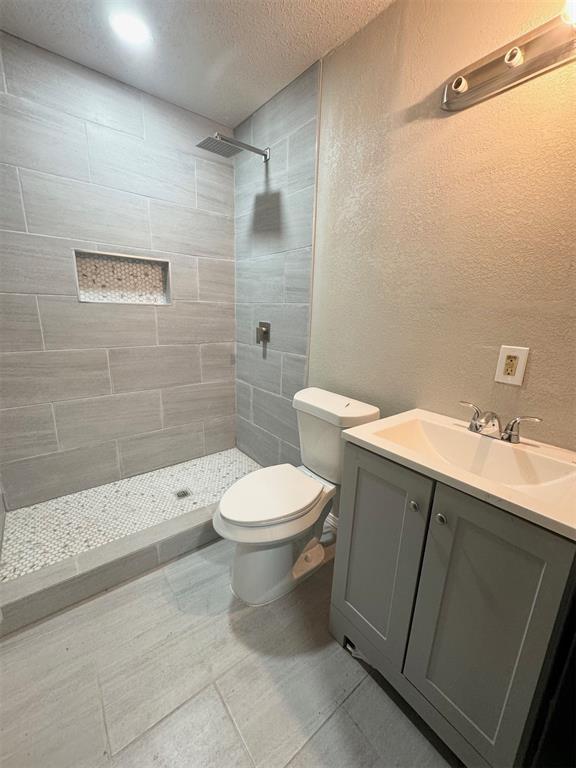 bathroom with vanity, a tile shower, a textured ceiling, and toilet