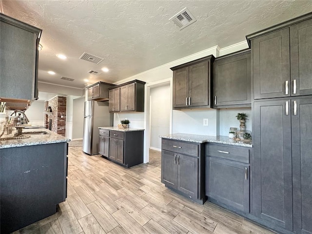 kitchen featuring dark brown cabinetry, a textured ceiling, stainless steel fridge, and light stone counters