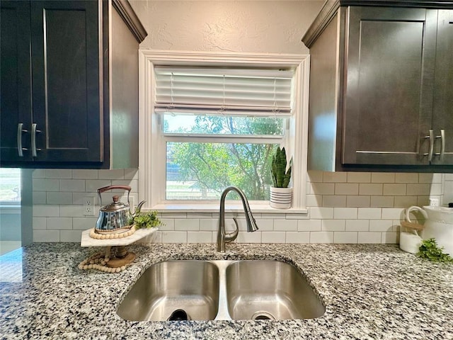 kitchen with tasteful backsplash, dark brown cabinetry, sink, and light stone counters