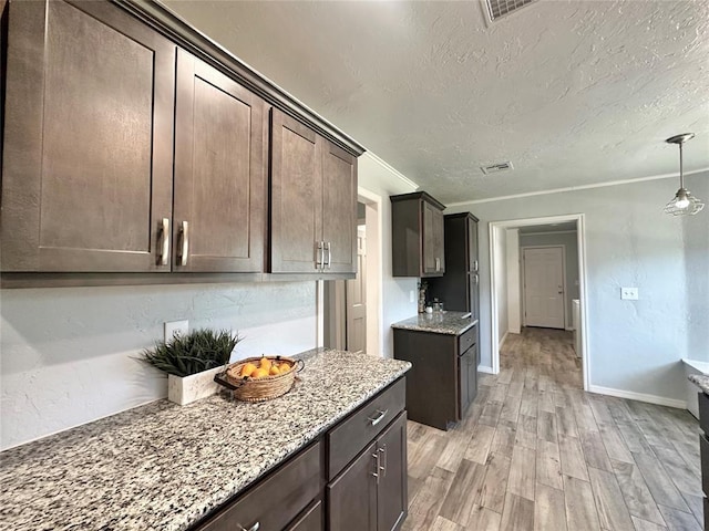 kitchen featuring hanging light fixtures, dark brown cabinets, a textured ceiling, light stone countertops, and light hardwood / wood-style floors