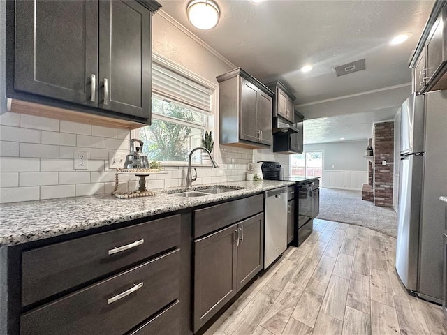 kitchen with appliances with stainless steel finishes, sink, backsplash, light stone countertops, and light hardwood / wood-style flooring