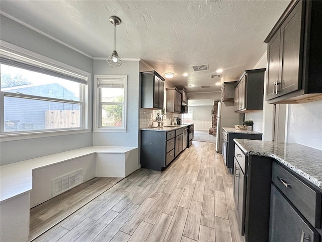 kitchen featuring hanging light fixtures, dark brown cabinetry, crown molding, a textured ceiling, and light wood-type flooring