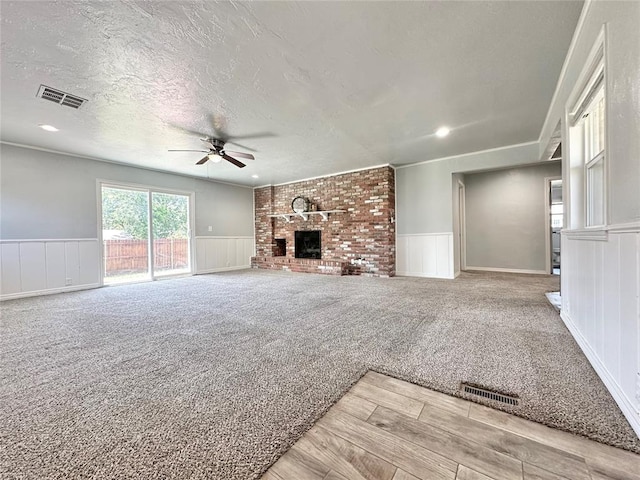 unfurnished living room featuring light carpet, a brick fireplace, a textured ceiling, and ceiling fan