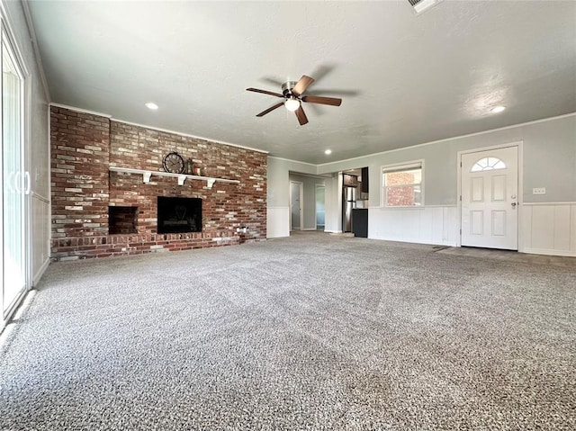 unfurnished living room featuring a fireplace, carpet flooring, ornamental molding, ceiling fan, and a textured ceiling