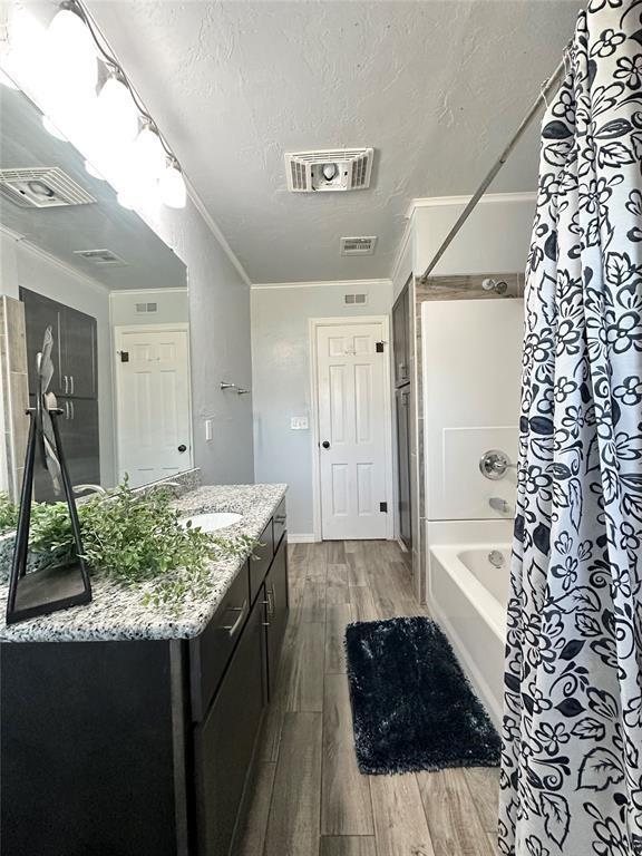 bathroom with crown molding, a textured ceiling, vanity, shower / bath combination with curtain, and hardwood / wood-style floors