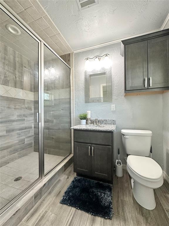 bathroom featuring vanity, toilet, a textured ceiling, and a shower with shower door