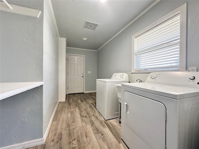 clothes washing area with ornamental molding, separate washer and dryer, and light hardwood / wood-style flooring