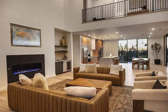 living room featuring sink, a towering ceiling, beverage cooler, and light hardwood / wood-style floors