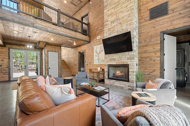 living room with a stone fireplace, wood walls, concrete floors, wooden ceiling, and a high ceiling