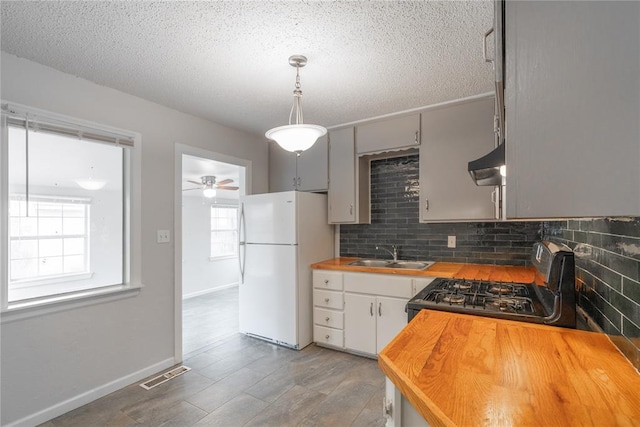 kitchen with wood counters, sink, gas stove, hanging light fixtures, and white refrigerator