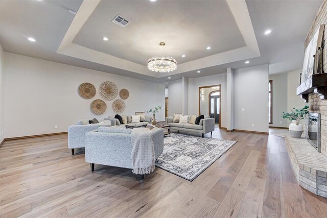 10401 Fawn Trace Rd, Mustang, OK 73064 - living area with a tray ceiling, visible vents, light wood-style floors, a chandelier, and a brick fireplace