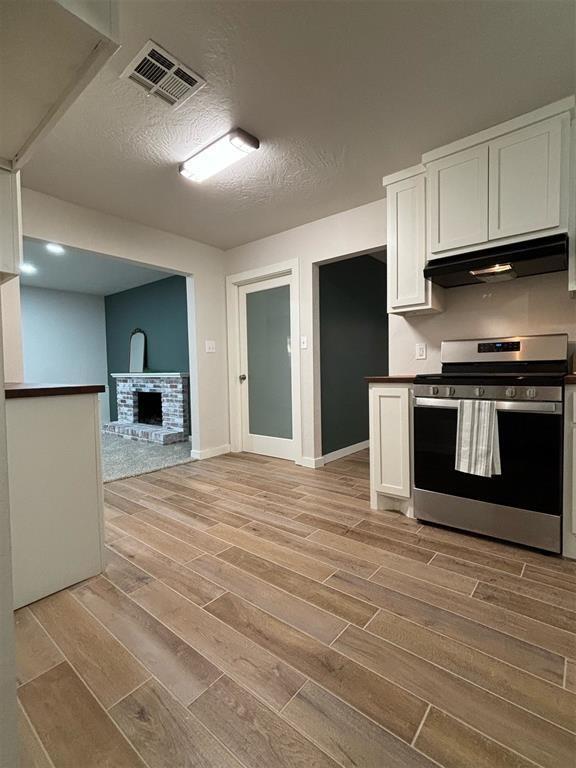 kitchen with white cabinets, a textured ceiling, stainless steel range oven, and a brick fireplace