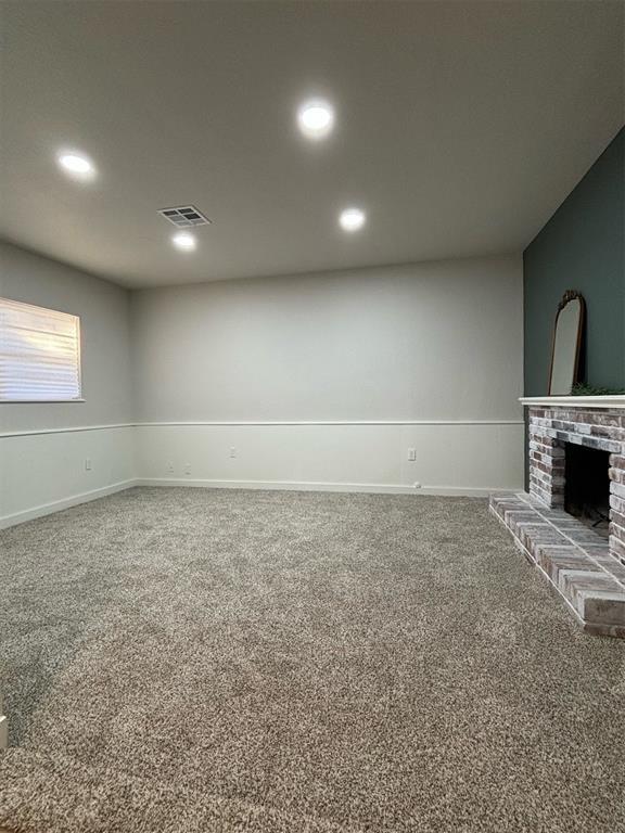 unfurnished living room featuring a brick fireplace and carpet