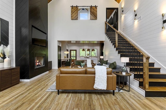 living room featuring a large fireplace, light hardwood / wood-style flooring, wood walls, and a towering ceiling