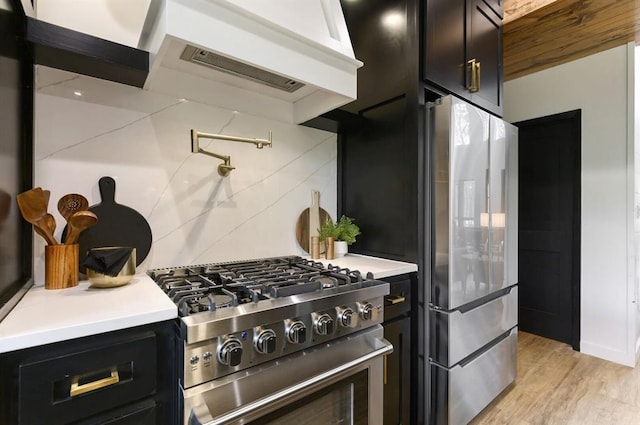 kitchen with stainless steel stove, tasteful backsplash, custom exhaust hood, fridge, and light hardwood / wood-style floors