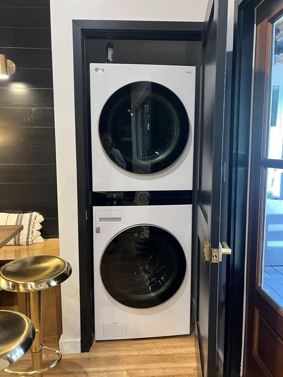 laundry room with hardwood / wood-style flooring, stacked washer and clothes dryer, and wooden walls