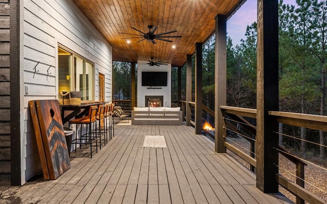 wooden deck with ceiling fan, an outdoor fireplace, and a bar