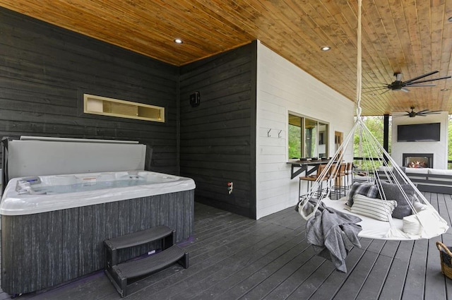 wooden deck with exterior fireplace, a hot tub, ceiling fan, and exterior bar