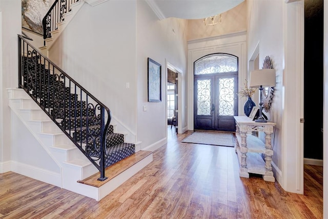 entryway featuring french doors, crown molding, hardwood / wood-style floors, and a high ceiling