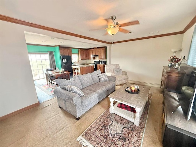 living area with baseboards, ornamental molding, a ceiling fan, and light colored carpet