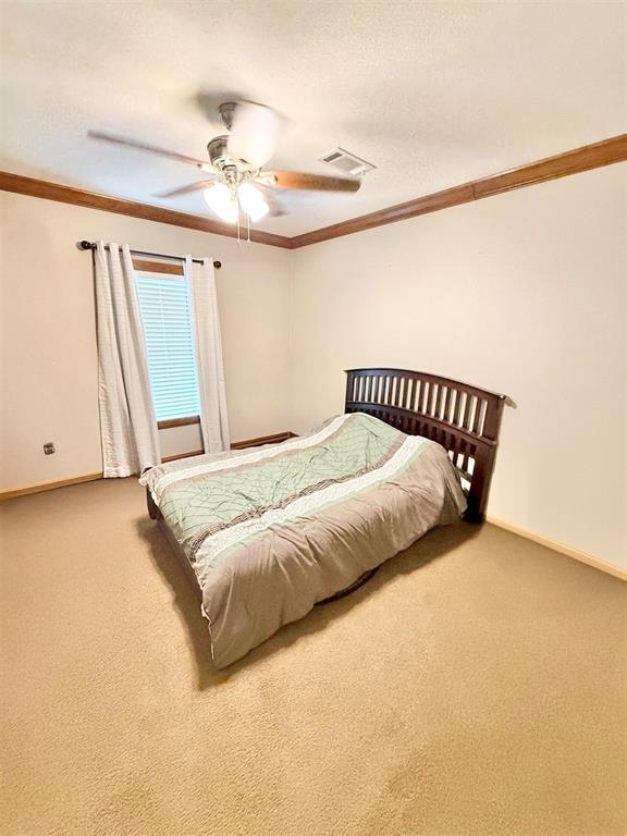 bedroom with carpet floors, a textured ceiling, visible vents, and crown molding