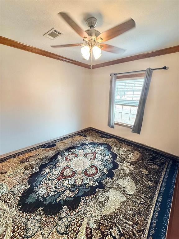 unfurnished room featuring a ceiling fan, visible vents, and crown molding