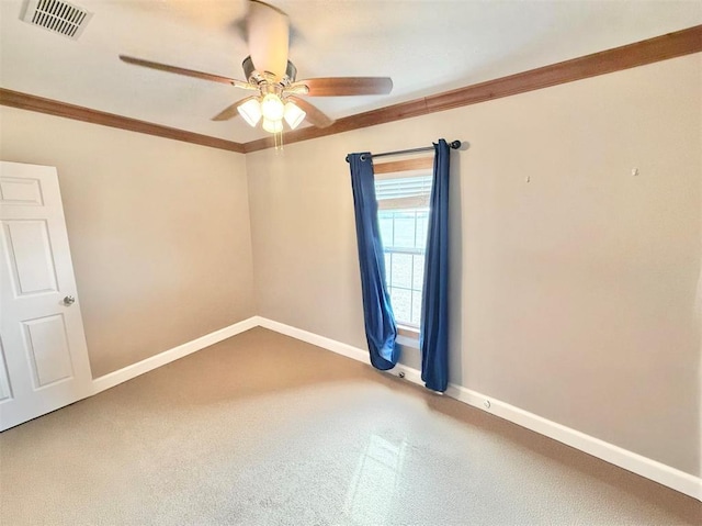 carpeted spare room with a ceiling fan, visible vents, crown molding, and baseboards