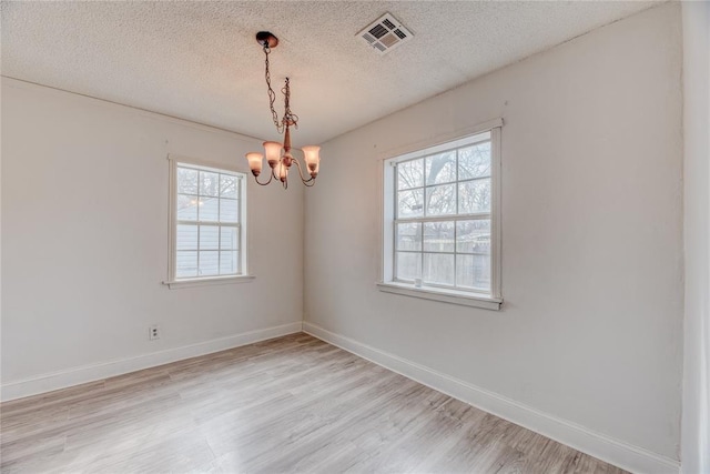 empty room featuring an inviting chandelier, light hardwood / wood-style floors, and a textured ceiling