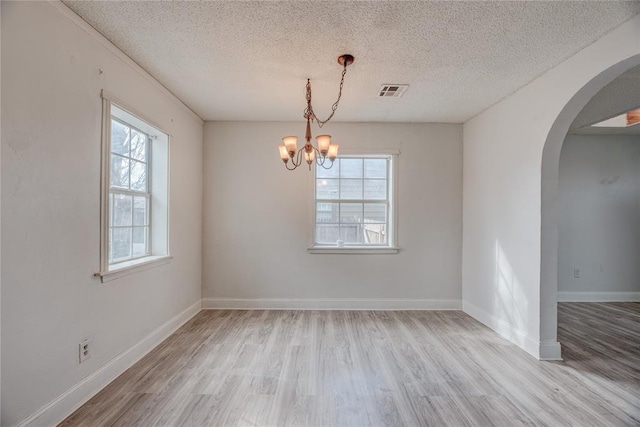 unfurnished room featuring a notable chandelier, light hardwood / wood-style floors, and a textured ceiling