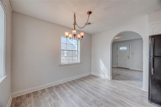 empty room with an inviting chandelier, light hardwood / wood-style flooring, and a textured ceiling