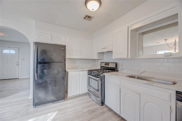 kitchen featuring stainless steel range with gas cooktop, black refrigerator, white cabinets, a textured ceiling, and light hardwood / wood-style flooring