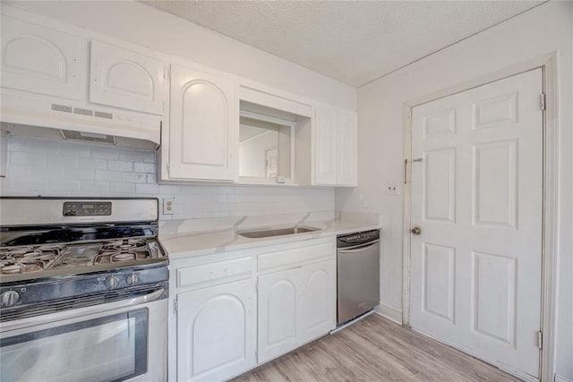 kitchen featuring sink, appliances with stainless steel finishes, light hardwood / wood-style floors, decorative backsplash, and white cabinets