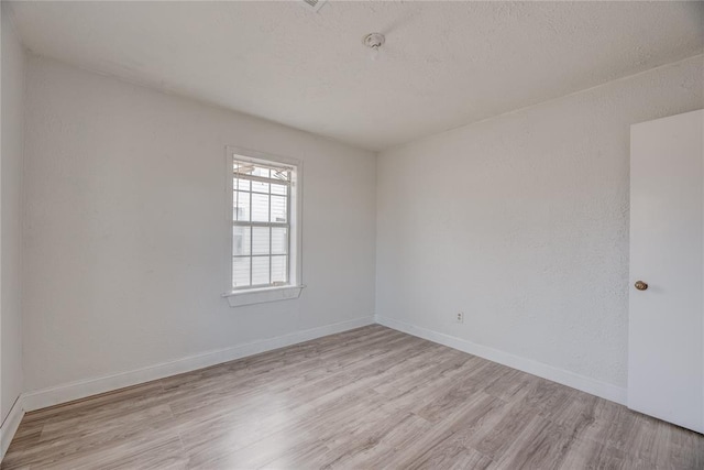 spare room featuring a textured ceiling and light hardwood / wood-style floors