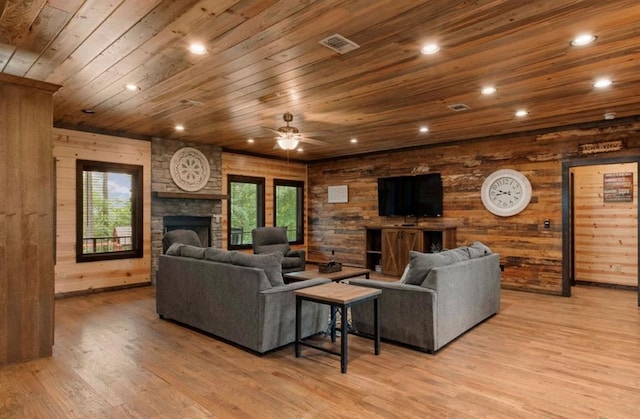 living room with wood ceiling, ceiling fan, wooden walls, a fireplace, and light wood-type flooring