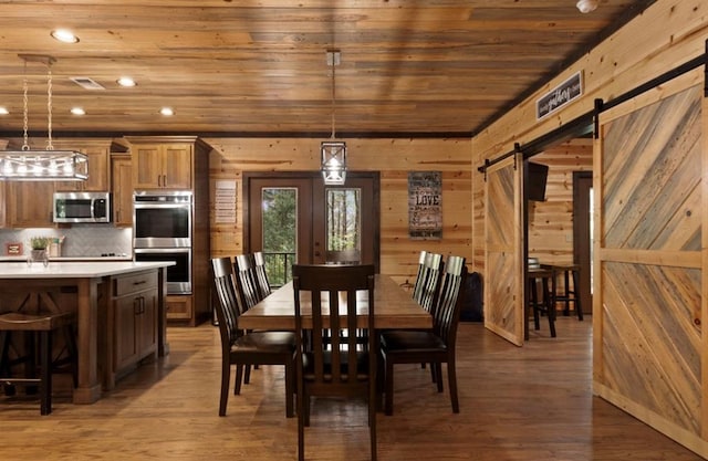 dining room with wood-type flooring, wooden ceiling, a barn door, and wooden walls