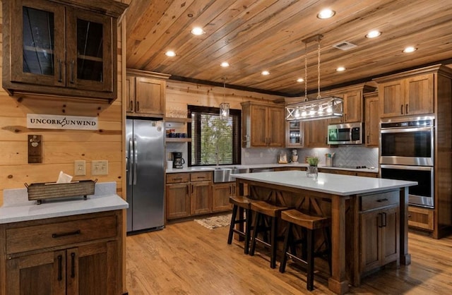 kitchen featuring a breakfast bar area, wood ceiling, decorative light fixtures, a center island, and appliances with stainless steel finishes