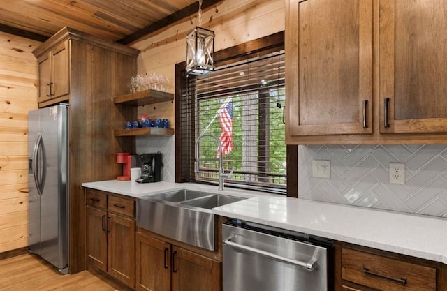 kitchen featuring appliances with stainless steel finishes, wood walls, decorative light fixtures, sink, and backsplash