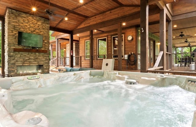 view of swimming pool featuring ceiling fan, an indoor hot tub, and an outdoor stone fireplace