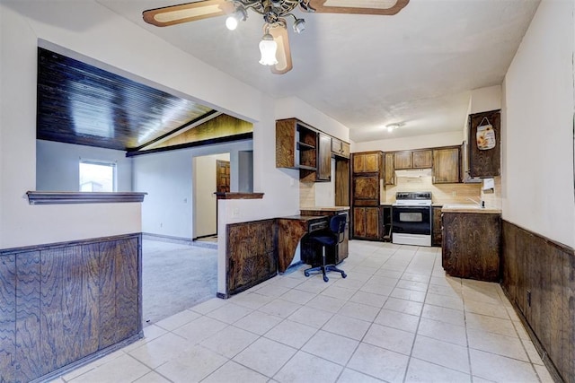 kitchen with electric stove, light tile patterned floors, dark brown cabinets, and wood walls