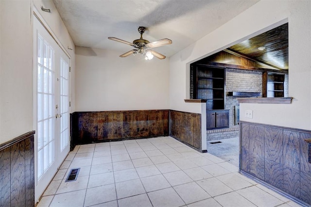 interior space featuring ceiling fan, light tile patterned floors, built in features, and wooden walls