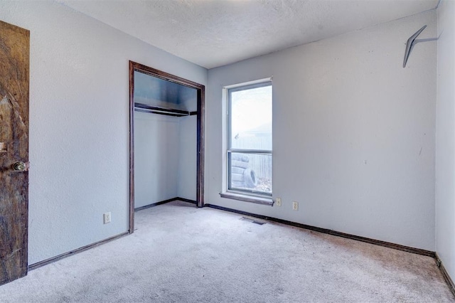 unfurnished bedroom featuring light colored carpet, a textured ceiling, and a closet