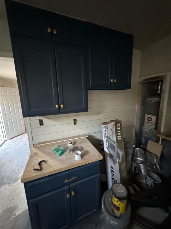 kitchen featuring wood counters, blue cabinetry, water heater, and wood walls