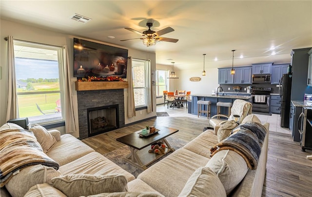 living room with ceiling fan, a fireplace, sink, and light wood-type flooring