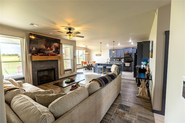 living room with sink, a stone fireplace, dark hardwood / wood-style floors, and ceiling fan