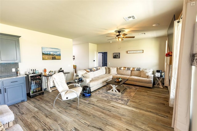 living room featuring wine cooler, dark wood-type flooring, ceiling fan, and bar area