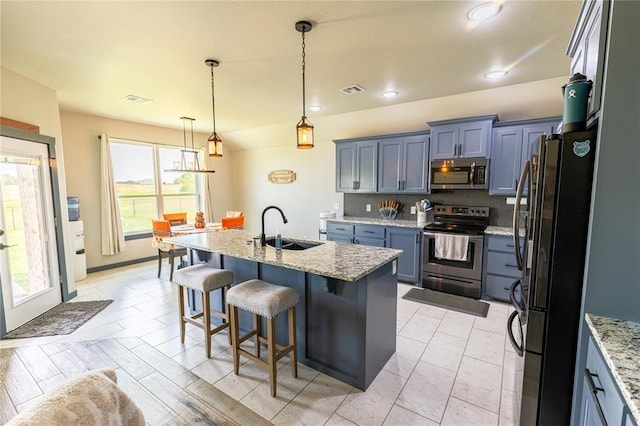 kitchen featuring sink, a kitchen island with sink, hanging light fixtures, stainless steel appliances, and light stone counters