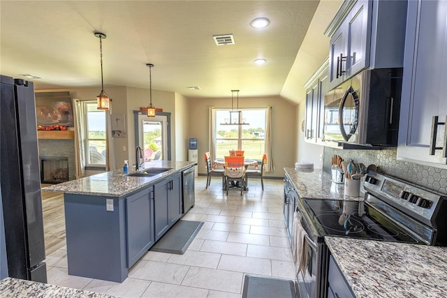 kitchen with pendant lighting, sink, light stone counters, stainless steel appliances, and a center island with sink